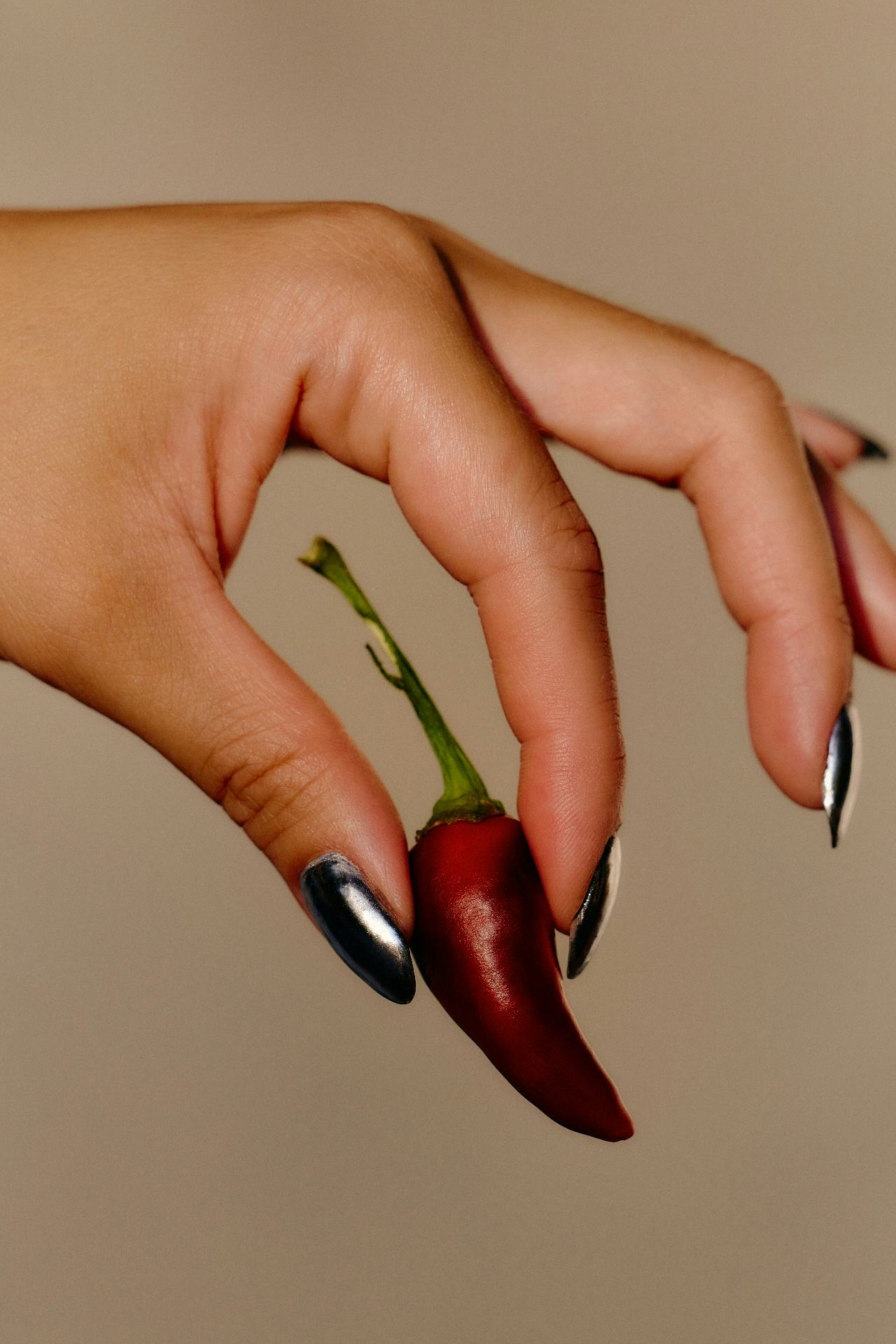 A hand with chrome nails holding a red chili